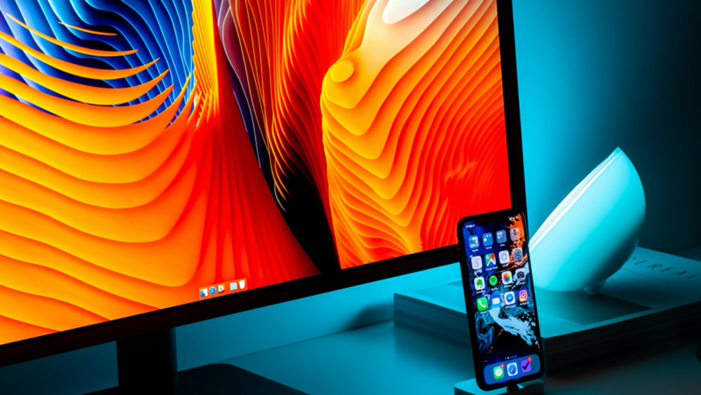 A smartphone on a stand in front of a colourful computer screen.